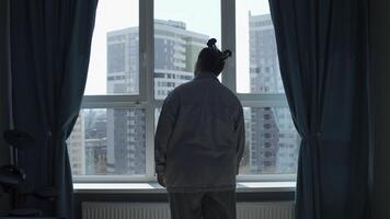 Young woman enjoying view through the panoramic window in the morning at home. Media. Girl in pajamas standing and thinking by the window in bedroom. photo