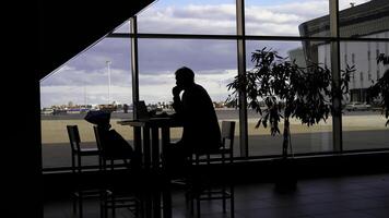 Businessman waiting for boarding at the airport and looking through panoramic windows. Silhouette of a man at a table with shadows of passing people. photo