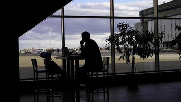 empresario esperando para embarque a el aeropuerto y mirando mediante panorámico ventanas silueta de un hombre a un mesa con oscuridad de paso gente. foto