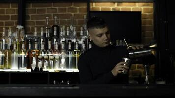 Young male bartender using shaker for the alcohol drink preparation. Action. Concept of party at night club. photo