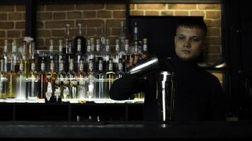 Young male bartender using shaker for the alcohol drink preparation. Action. Concept of party at night club. photo