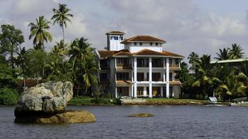 The view of mansion on the shore with palm trees. Action. Living at the sea shore with green vegetation. photo
