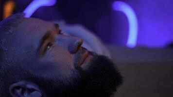 Close up side view of a bearded man looking up and thinking of something. Media. Young man with neon light on the background. photo