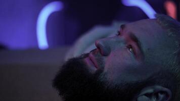 Close up side view of a bearded man looking up and thinking of something. Media. Young man with neon light on the background. photo