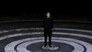 alto hombre en negro ropa en pie en el entrometerse de anfiteatro. valores acortar. asfalto de colores en negro círculos foto