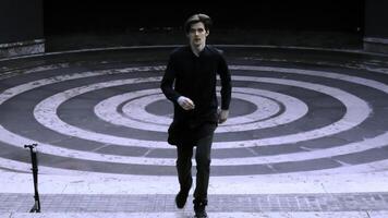 Young man dressed in black running up the stairs of stone amphitheater. Stock clip. Asphalt painted in white and black rings. photo