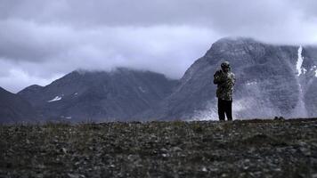 Man photographing mountain highness landscape. Clip. Rear view of a man hiker taking photos of heavy clouds and mountain tops.