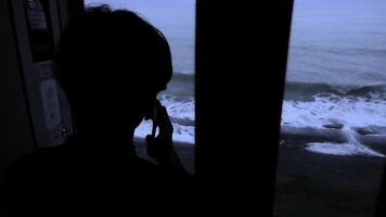 Young man standing next to a train window and looking outside Stock clip. Man with smartphone looking through the window on sea. photo