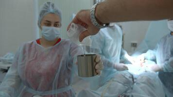 Pouring sterile liquid into the small container in the operating room. Action. Team of medical workers. video