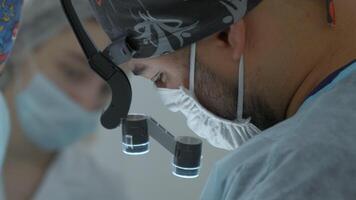 chirurgien tête avec professionnel des lunettes à en fonctionnement chambre. action. proche en haut côté vue de une médecin dans des lunettes avec binoculaire loupes. video