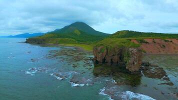 Top view of rocky coast with algae on shore. Clip. Landscape of rocks on coast with algae on background of mountains in cloudy weather. Diversity of flora of sea coast with rocky mountains video