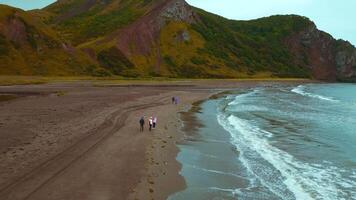 Top view of people by sea with mountain view. Clip. Coast with walking people and amazing mountains on cloudy day. Walk on mountain coast of ocean on cloudy day video