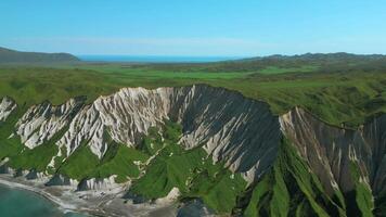 Green slopes meeting blue ocean aerial view. Clip. White cliffs and blue shore against clear blue sky. video