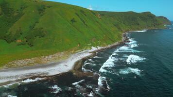 Wild nature, green mountains with steep green slopes leading to the sea. Clip. Aerial of foam of blue waves break in volcanic rocks. video