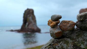 de cerca de apilado rocas en playa con rocas acortar. piedras apilado en composición en borroso antecedentes de rocas en mar. piedras apilado en torreta estar en antecedentes de nublado mar video