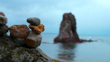 Close-up of stacked rocks on beach with rocks. Clip. Stones stacked in composition on blurred background of rocks in sea. Stones stacked in turret stand on background of overcast sea video