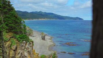 Beautiful view of bend of coast with rocks on sunny day. Clip. Landscape of rocky coast with green mountains and forest. Beautiful beach with rocks and blue sea on sunny day video