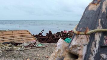 Ruins of fishing boats and garbage on seashore. Clip. Garbage and ruins of sea boats on shore on cloudy day. Debris and destroyed boats after storm on seashore video