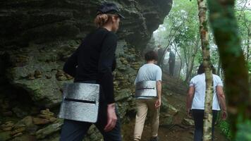 Group of tourists is walking along mountain trail in forest. Clip. Active tourists walk along trail in dense forest with rocks. Tourists go on difficult hiking route in forest with rocks video