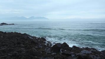 mar rocas con Moviente olas en antecedentes nublado horizonte. acortar. rocoso rocas palo fuera en agua en costa en nublado día. hermosa marina con rocas en nublado clima video