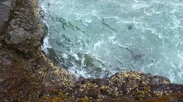 Close-up of surge of waves on rocky shore. Clip. Beautiful waves with splash roll on stones of seashore. Beautiful splashes of waves crashing on rocks on cloudy day video