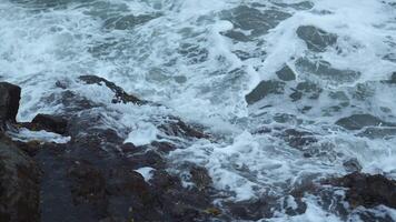 de cerca de oleada de olas en rocoso costa. acortar. hermosa olas con chapoteo rodar en piedras de costa. hermosa salpicaduras de olas estrellarse en rocas en nublado día video