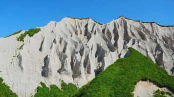 increíble blanco montañas con verde césped. acortar. hermosa patrones en rocoso blanco montaña con brillante verdor en soleado verano día. blanco rocas de volcánico origen en isla en verano día video