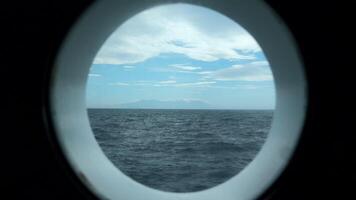 Aussicht von runden Deck Fenster zu Meer. Clip. schön Seelandschaft mit Berg Küste auf Horizont von runden Fenster. Meer Reise und Aussicht von runden Fenster video