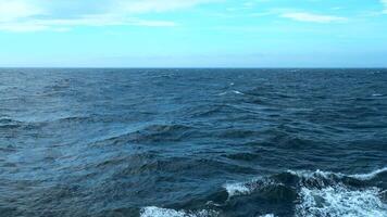 Beautiful view of horizon of blue sea with waves. Clip. Foam from waves of floating ship in blue sea. In blue sea with waves on background horizon with blue sky video