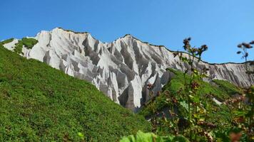 Fantastisk vit bergen med grön gräs. klämma. skön mönster på klippig vit berg med ljus grönska på solig sommar dag. vit stenar av vulkanisk ursprung på ö på sommar dag video