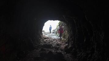 View from cave to tourists. Clip. Rear view of man coming out of cave. Tourist comes out of cave into light video