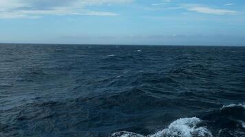 Beautiful view of horizon of blue sea with waves. Clip. Foam from waves of floating ship in blue sea. In blue sea with waves on background horizon with blue sky video