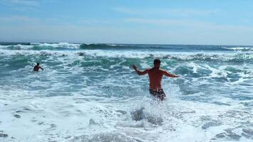 mensen baden in mooi blauw golven Aan zonnig dag. klem. mooi blauw golven met schuim Aan kust met vakantie mensen. mensen in zwemkleding zwemmen met blauw golven van zee Aan zomer dag video