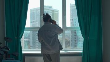 Rear view of a woman talking on a cell phone by the window. Media. Woman in pajamas talking on smartphone at home. video