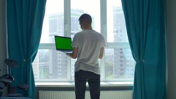 Back view of a young man in white t shirt working on laptop with green chroma key screen. Media. Concept of using modern technologies for remote work. video