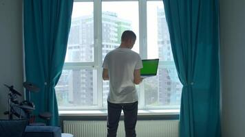 jovem homem trabalhando a partir de lar, conceito do freelance. meios de comunicação. homem segurando computador portátil com verde croma chave tela e digitando. video