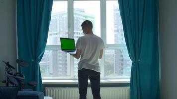 Back view of a young man in white t shirt working on laptop with green chroma key screen. Media. Concept of using modern technologies for remote work. video