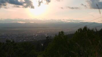 bellissimo Visualizza di città con cavo macchina. clip. paesaggio di città nel valle su sfondo di montagna orizzonte con sole. nuvoloso tempo metereologico con sole è al di sopra di valle con cittadina e cavo auto video