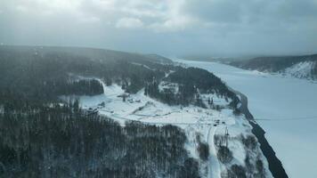 aérien vue de scénique la nature dans hiver saison avec petit village et rivière. agrafe. en volant neige et le hiver du froid Soleil brillant sur pin arbre forêt. video