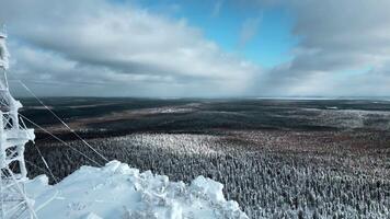 en flyg över de tät vinter- sibirisk skog i de eftermiddag. klämma. vit berg och en frysta väder torn på dess topp. video