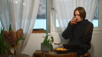 Young man drinks tea and looks at tablet in cafe. Media. Handsome young man is drinking tea alone and looking at tablet. Student is relaxing with tablet in cozy cafe video