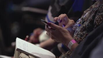 Girl with notepad sits in conference room and scrolls the screen. Stock. Closeup of female hands are typing sms on smartphone. Closeup of female hands scrolling something in the smart phone video