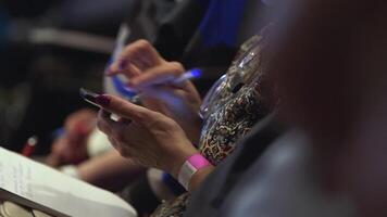 Girl with notepad sits in conference room and scrolls the screen. Stock. Closeup of female hands are typing sms on smartphone. Closeup of female hands scrolling something in the smart phone video