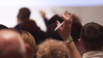 View from behind of a large mixed ethnicity group of people in a classroom, listening as their lector holds a lecture. Stock. People puts up his hand to ask a question video