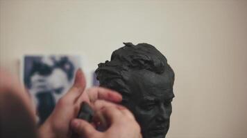 Sculptor is working on the creation of a monument. Clip. Sculptor smears clay on bust with his finger, only hands are visible video