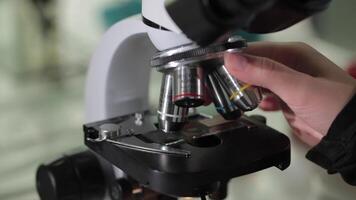 vicino su di l'esame di test campione sotto il microscopio nel laboratorio. vicino su di microscopio a il sangue laboratorio. microscopio a laboratorio e mani di il scienziato vicino su video