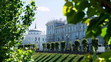 Central street of the city with adorable white houses and many green trees on blue cloudy sky background. Stock footage. Summer in the city, architecture concept. video