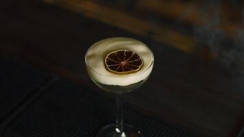 Close up of beautiful cocktail with thick foam and dried orange slice. Media. Beverage on bar counter background. video