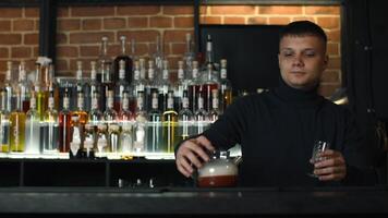 Close up of bartender at a bar counter pouring alcohol into vintage glass. Media. Pouring red hot alcoholic tincture with steam. video