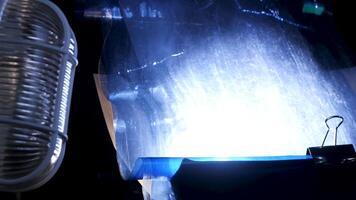 Close up of blue plastic sheet under the white old fashioned glass lamp light on black background. Stock footage. Creating of unusual background for photo and video shooting